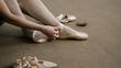 © Framestock - Ballerina sits on floor at dance studio and puts on pointe shoes before choreography lesson. Graceful ballet dancer prepares for performance or training. Classical ballet dance school. Feet close up.