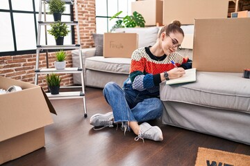 Wall Mural - Young woman writing on notebook sitting on floor at new home