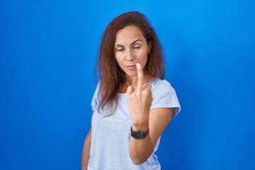 Sticker - Brunette woman standing over blue background showing middle finger, impolite and rude fuck off expression