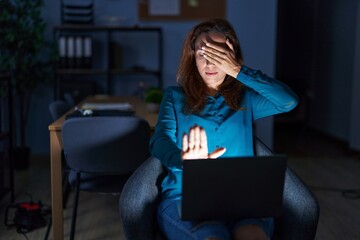 Canvas Print - Brunette woman working at the office at night covering eyes with hands and doing stop gesture with sad and fear expression. embarrassed and negative concept.