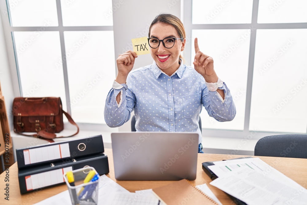 Young hispanic business woman at the office calculating taxes surprised ...