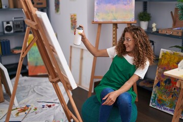 Young beautiful hispanic woman artist smiling confident using graffiti spray drawing at art studio