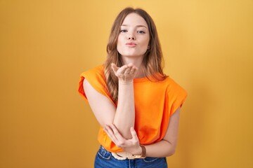 Wall Mural - Caucasian woman standing over yellow background looking at the camera blowing a kiss with hand on air being lovely and sexy. love expression.