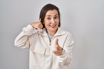 Poster - Middle age hispanic woman standing over isolated background smiling doing talking on the telephone gesture and pointing to you. call me.