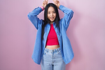 Sticker - Young asian woman standing over pink background posing funny and crazy with fingers on head as bunny ears, smiling cheerful