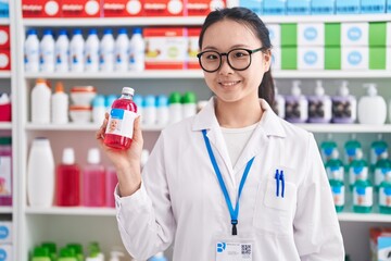 Canvas Print - Young chinese woman pharmacist smiling confident holding medication bottle at pharmacy