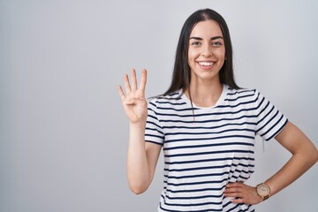 Sticker - Young brunette woman wearing striped t shirt showing and pointing up with fingers number four while smiling confident and happy.