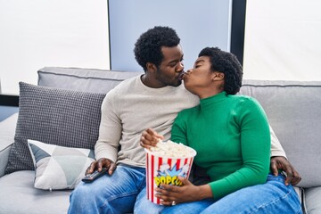 Wall Mural - African american man and woman couple watching movie eating popcorn kissing at home