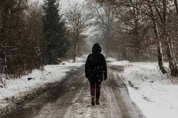 walking person in black jacket on the country road on a sad snowy winter day