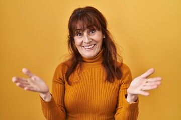 Canvas Print - Middle age hispanic woman standing over yellow background smiling cheerful offering hands giving assistance and acceptance.