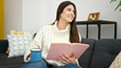 © Krakenimages.com - Young beautiful hispanic woman reading book and drinking coffee sitting on sofa at home