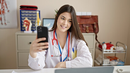 Canvas Print - Young beautiful hispanic woman doctor using laptop and smartphone at clinic