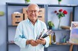 © Krakenimages.com - Senior grey-haired man artist smiling confident holding paintbrushes at art studio