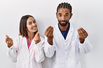 Canvas Print - Young hispanic doctors standing over white background doing money gesture with hands, asking for salary payment, millionaire business