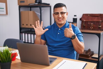 Sticker - Young hispanic man working at the office with laptop showing and pointing up with fingers number six while smiling confident and happy.