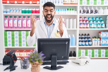 Wall Mural - Hispanic man with beard working at pharmacy drugstore celebrating mad and crazy for success with arms raised and closed eyes screaming excited. winner concept