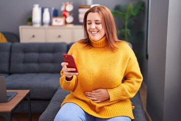 Wall Mural - Young beautiful plus size woman watching video on smartphone sitting on sofa at home