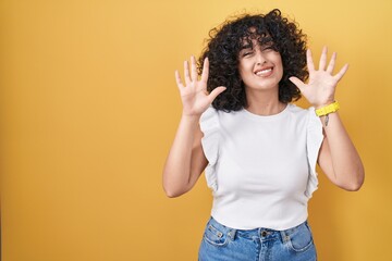 Sticker - Young middle east woman standing over yellow background showing and pointing up with fingers number ten while smiling confident and happy.