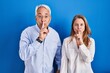 © Krakenimages.com - Middle age hispanic couple standing over blue background asking to be quiet with finger on lips. silence and secret concept.