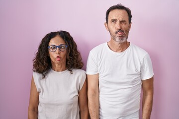 Wall Mural - Middle age hispanic couple together over pink background making fish face with lips, crazy and comical gesture. funny expression.