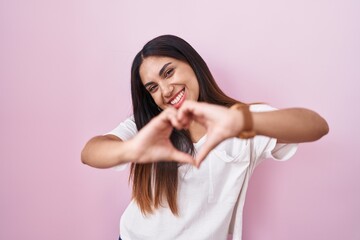 Wall Mural - Young arab woman standing over pink background smiling in love doing heart symbol shape with hands. romantic concept.