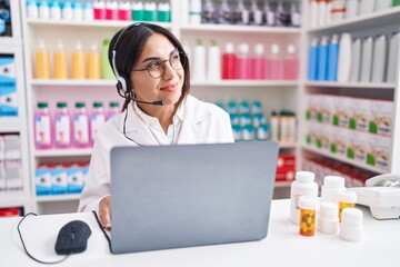 Wall Mural - Young arab woman working at pharmacy drugstore using laptop looking away to side with smile on face, natural expression. laughing confident.