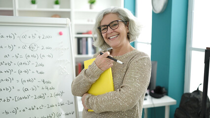 Middle age woman with grey hair teacher teaching maths lesson holding book at university classroom