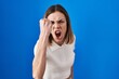 © Krakenimages.com - Hispanic woman standing over blue background angry and mad raising fist frustrated and furious while shouting with anger. rage and aggressive concept.