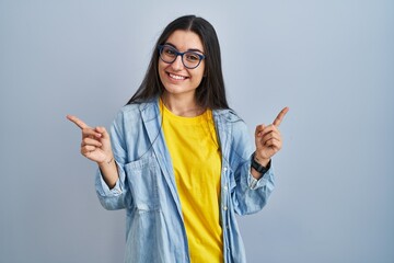 Poster - Young hispanic woman standing over blue background smiling confident pointing with fingers to different directions. copy space for advertisement