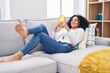 © Krakenimages.com - Young hispanic woman using smartphone lying on sofa at home