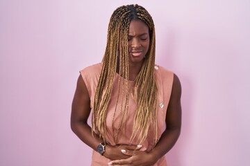 Wall Mural - African american woman with braided hair standing over pink background with hand on stomach because indigestion, painful illness feeling unwell. ache concept.