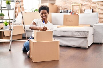 Wall Mural - African american woman writing on package sitting on floor at new home