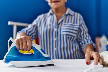 Wall Mural - Senior grey-haired woman smiling confident ironing clothes at laundry room