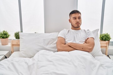 Wall Mural - Young hispanic man with serious expression sitting on bed at bedroom