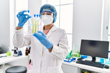 Poster - Young latin woman wearing scientist uniform holding test tube at laboratory