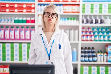 Poster - Young caucasian woman working at pharmacy drugstore puffing cheeks with funny face. mouth inflated with air, crazy expression.