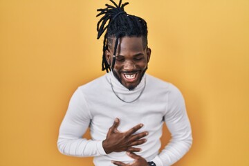 Wall Mural - African man with dreadlocks wearing turtleneck sweater over yellow background smiling and laughing hard out loud because funny crazy joke with hands on body.