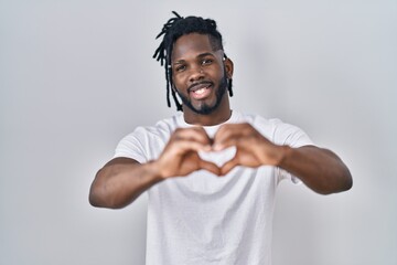 Poster - African man with dreadlocks wearing casual t shirt over white background smiling in love doing heart symbol shape with hands. romantic concept.