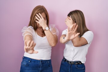 Poster - Hispanic mother and daughter wearing casual white t shirt over pink background covering eyes with hands and doing stop gesture with sad and fear expression. embarrassed and negative concept.