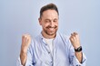 © Krakenimages.com - Middle age caucasian man standing over blue background very happy and excited doing winner gesture with arms raised, smiling and screaming for success. celebration concept.