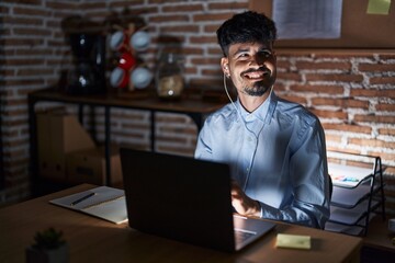 Sticker - Young hispanic man with beard working at the office at night looking away to side with smile on face, natural expression. laughing confident.