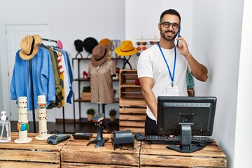 Sticker - Young hispanic man shopkeeper talking on the smartphone working at clothing store