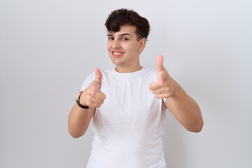 Poster - Young non binary man wearing casual white t shirt pointing fingers to camera with happy and funny face. good energy and vibes.