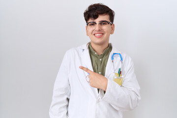 Canvas Print - Young non binary man wearing doctor uniform and stethoscope cheerful with a smile of face pointing with hand and finger up to the side with happy and natural expression on face