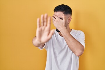 Wall Mural - Young handsome man wearing casual t shirt over yellow background covering eyes with hands and doing stop gesture with sad and fear expression. embarrassed and negative concept.