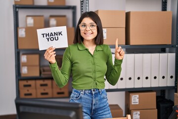 Wall Mural - Young hispanic doctor woman working at small business ecommerce holding thank you banner smiling with an idea or question pointing finger with happy face, number one