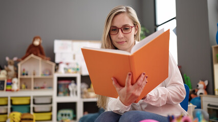 Poster - Young blonde woman preschool teacher smiling confident reading book at kindergarten