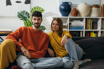 Wall Mural - Front view of a young Caucasian couple sitting on the sofa at home