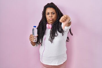 Canvas Print - Plus size hispanic woman wearing sportswear and headphones looking unhappy and angry showing rejection and negative with thumbs down gesture. bad expression.