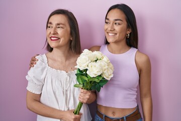 Wall Mural - Hispanic mother and daughter holding bouquet of white flowers looking away to side with smile on face, natural expression. laughing confident.